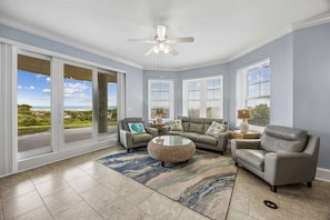 A spacious living room with a large sliding glass door leading to a balcony, a ceiling fan, and a round coffee table.