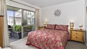 Un dormitorio con una cama grande, una puerta corrediza al exterior, dos mesitas de noche con lámparas y un adorno en la pared.