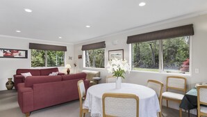 Una habitación con un sofá rojo, una mesa de comedor redonda con sillas y ventanas grandes con cortinas.