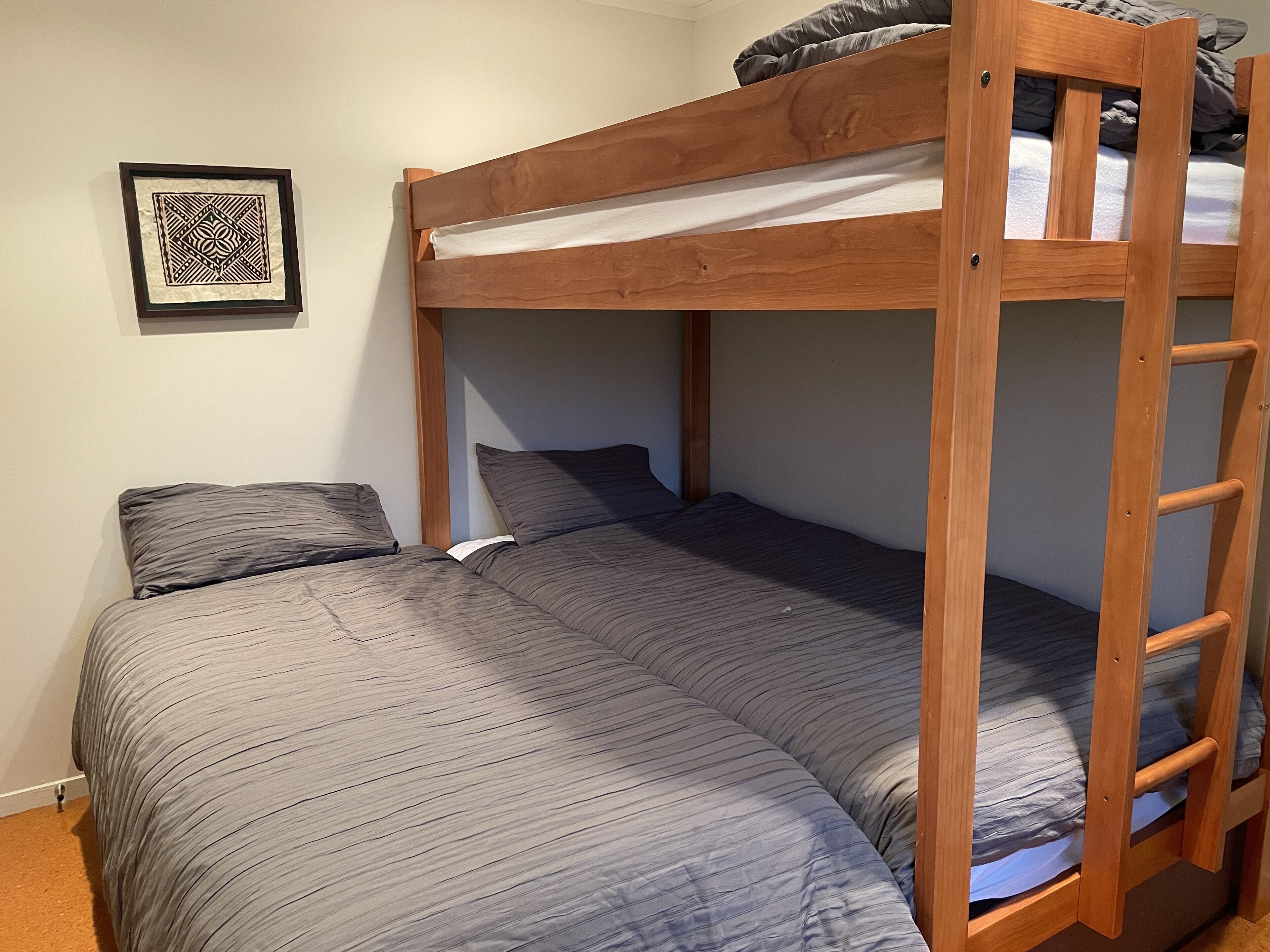 A bunk bed with a wooden frame, grey bedding, and a ladder.