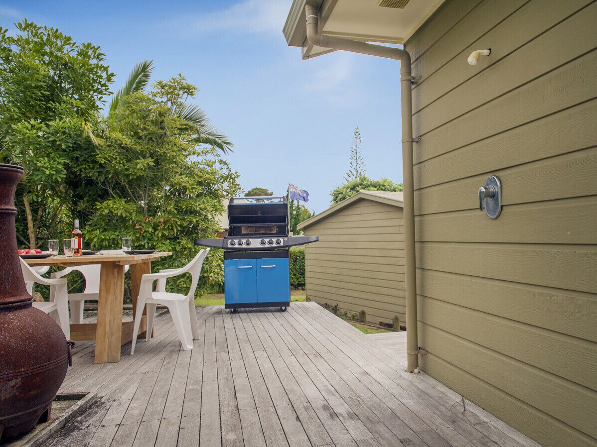 A backyard with a barbecue grill, a wooden deck, a table with chairs, and a large vase.