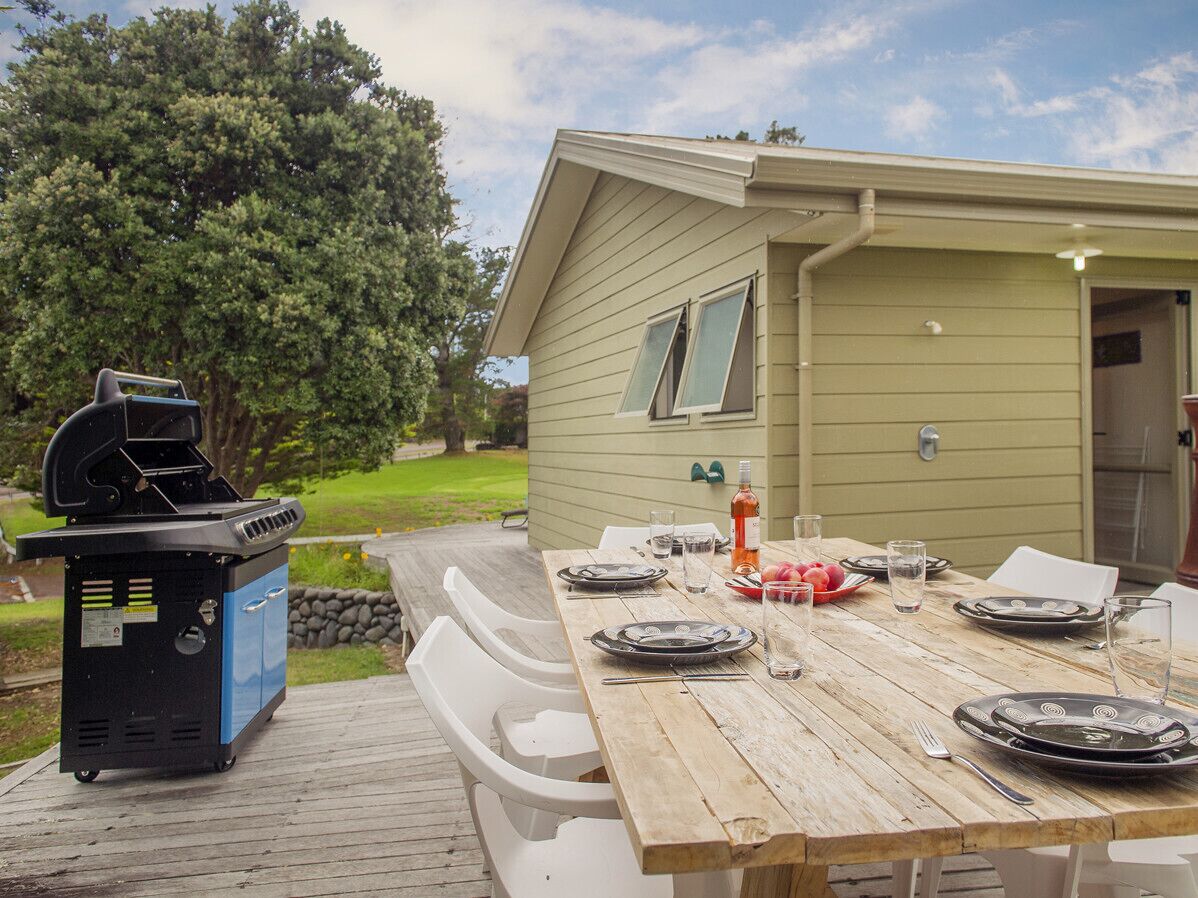 Een houten terras met een barbecue en een eettafel, klaar voor een maaltijd buiten.