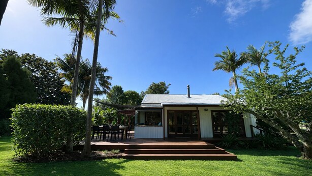 A house with a covered patio, surrounded by lush greenery and palm trees. - Matapouri Hideaway - Matapouri Holiday Home (Matapouri)