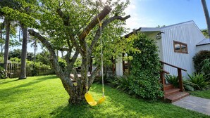 A tree with a swing, a white building, and a well-maintained lawn. - Matapouri Hideaway - Matapouri Holiday Home (Matapouri)