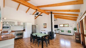 A spacious kitchen with modern appliances, a dining area with a table and chairs, and a living area with a sofa and a TV. - Matapouri Hideaway - Matapouri Holiday Home (Matapouri)