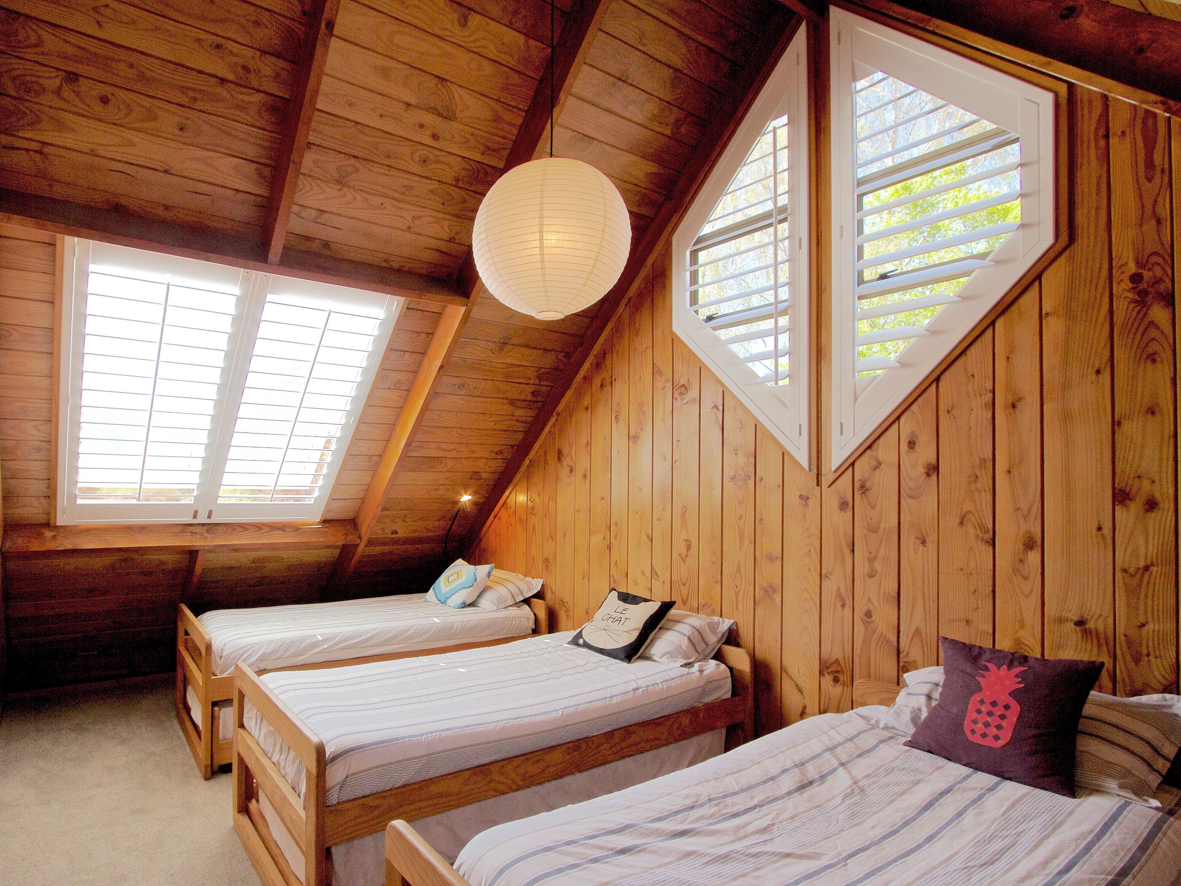 A wooden room with two beds, a slanted ceiling, and large windows.
