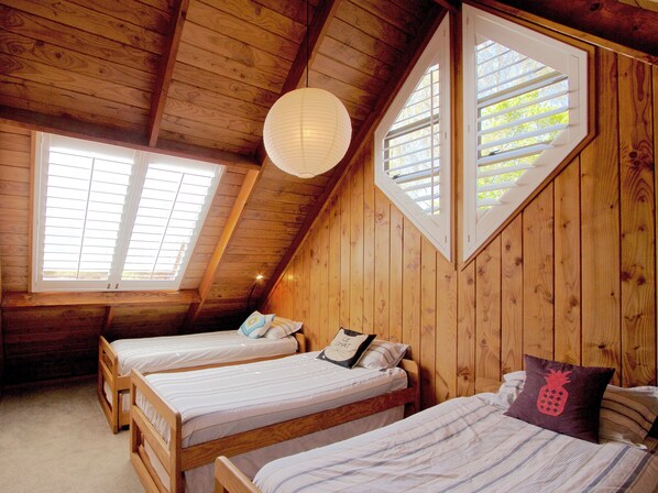 Una habitación de madera con dos camas, techo inclinado y ventanas amplias.