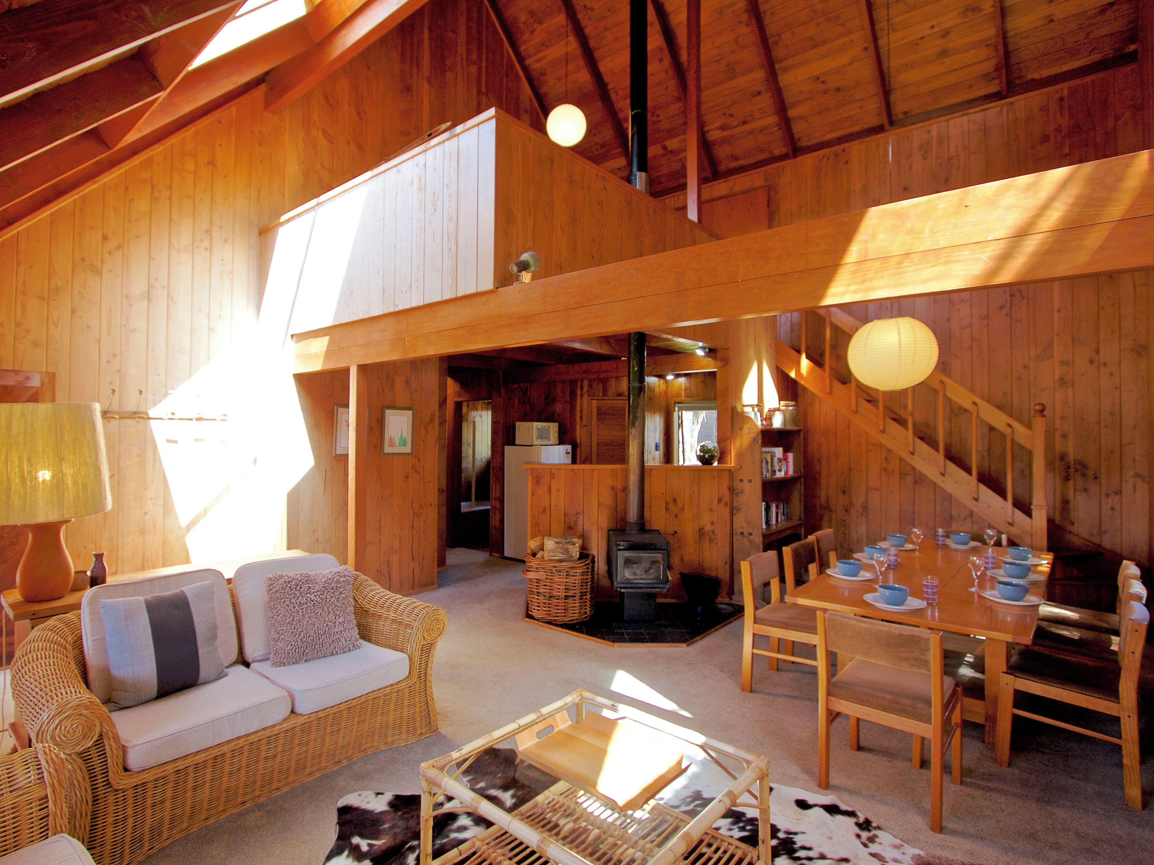 A cozy wooden cabin interior with a sofa, dining table, and a fireplace.