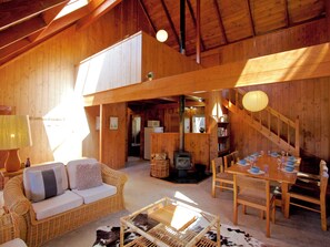 Acogedor interior de cabaña de madera con sofá, mesa de comedor y chimenea.