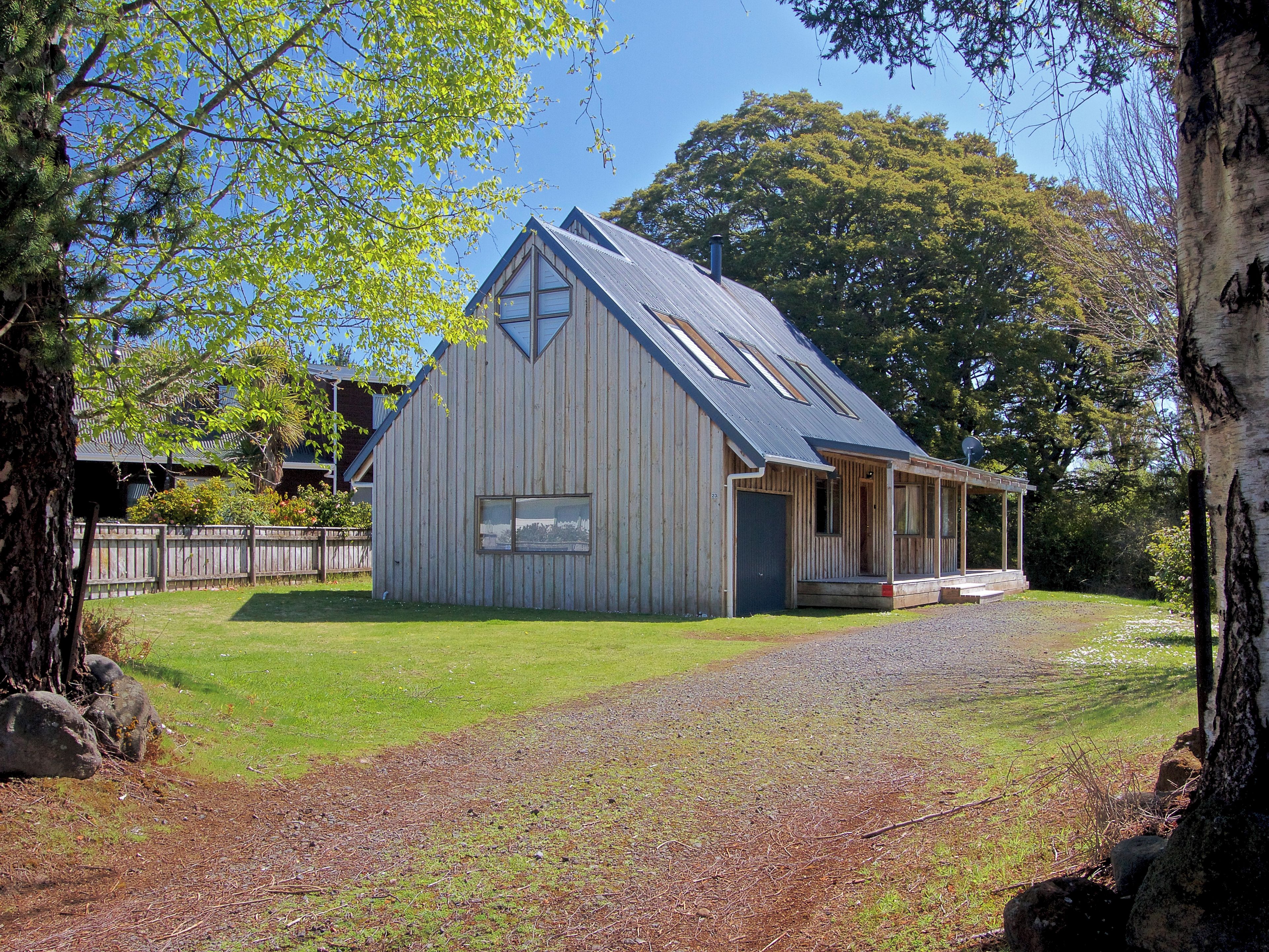 A rustic wooden building with a sloped roof, a porch, and a gravel driveway.