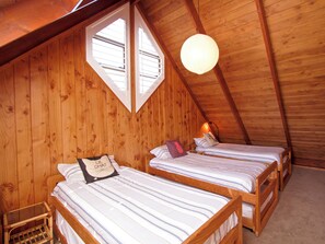 Une chambre mansardée chaleureuse, avec deux lits superposés en bois, une petite chaise en bois et un seul luminaire suspendu.