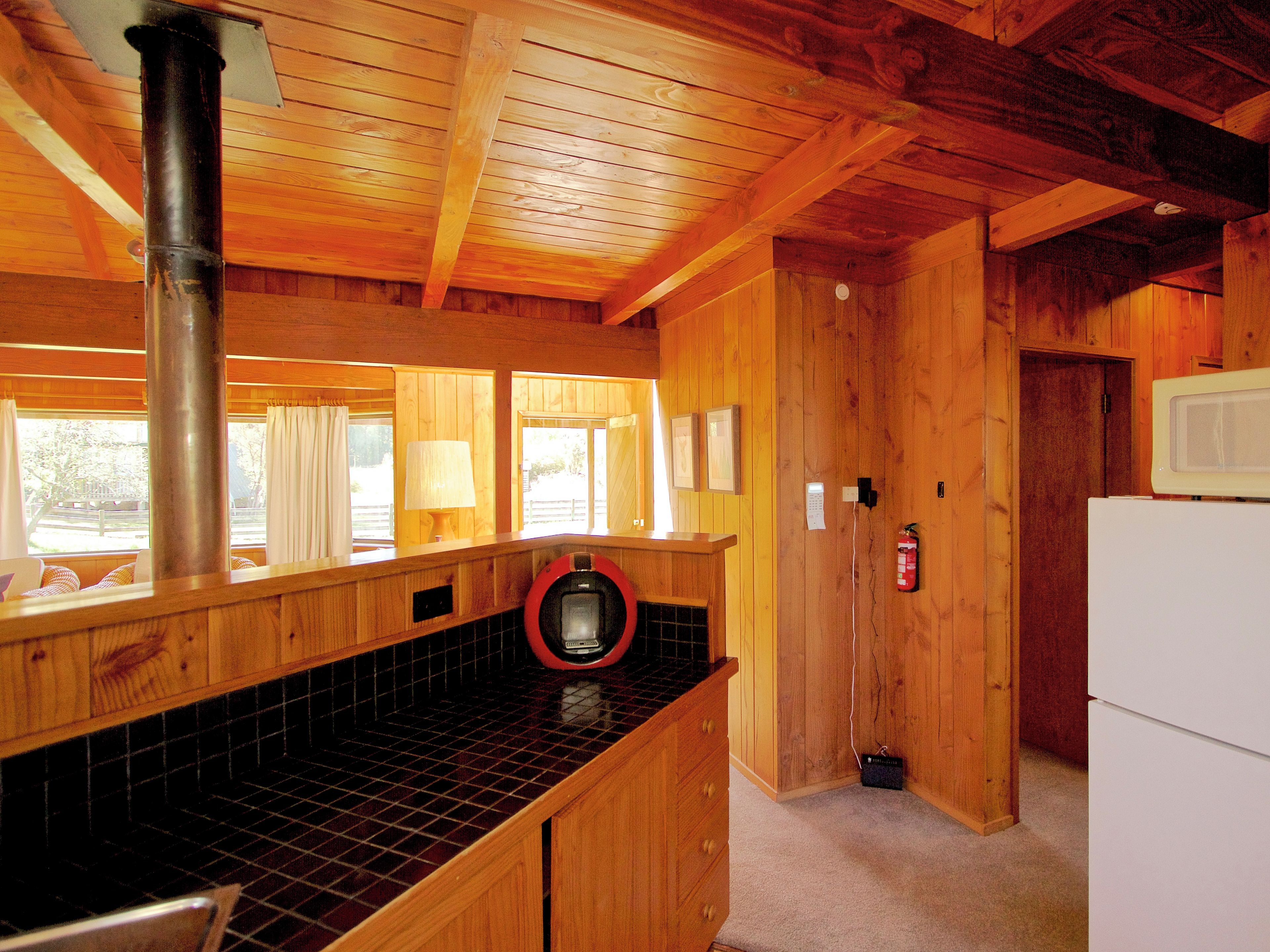 A wooden cabin interior with a kitchen area, including a stove, sink, and tiled backsplash.