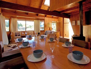 Un interior de madera con una mesa de comedor preparada para cuatro personas, rodeada de sofás y una chimenea.