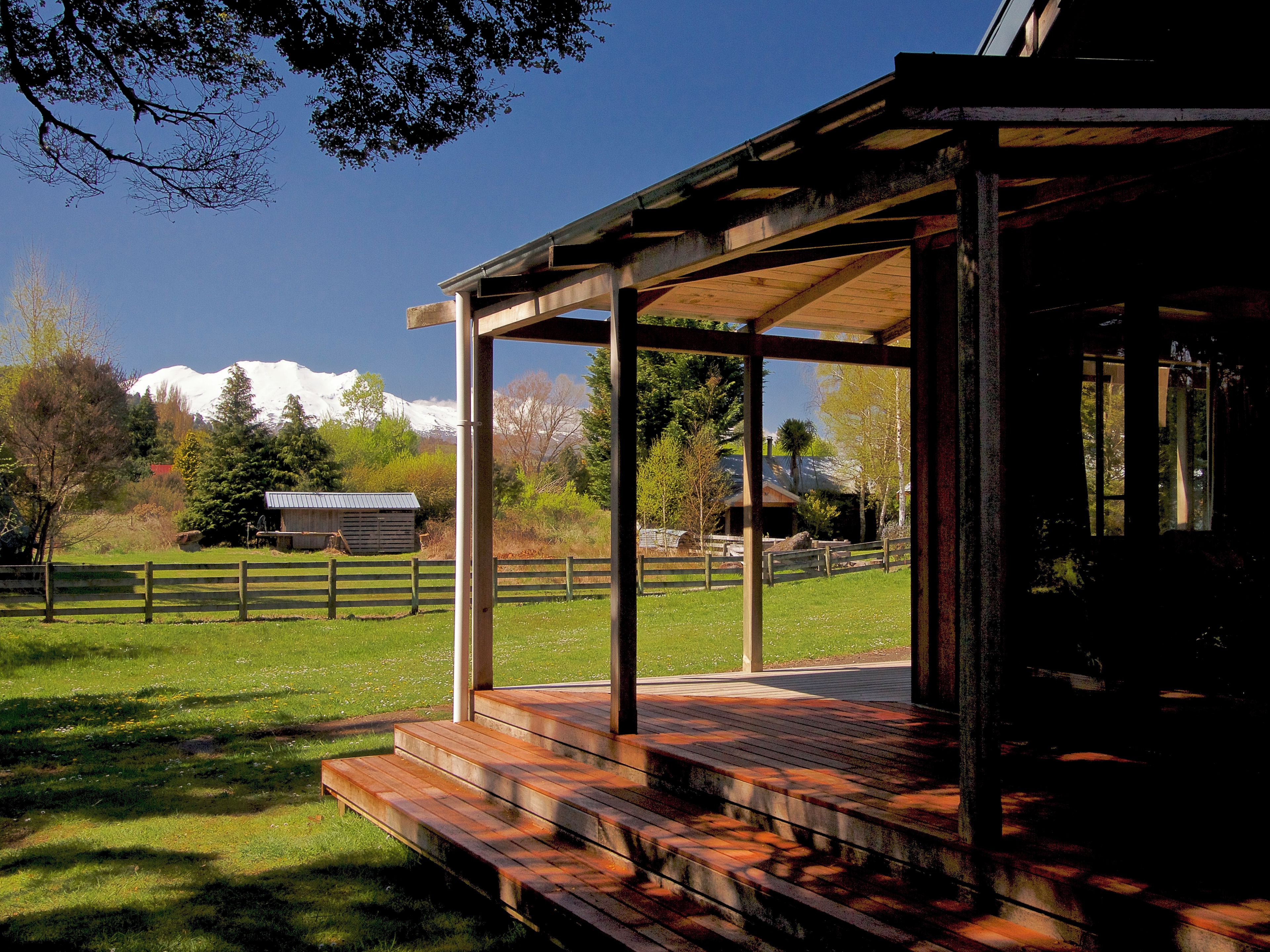 A covered outdoor area with wooden steps leading to a porch, surrounded by a fenced property with a mountain in the background.