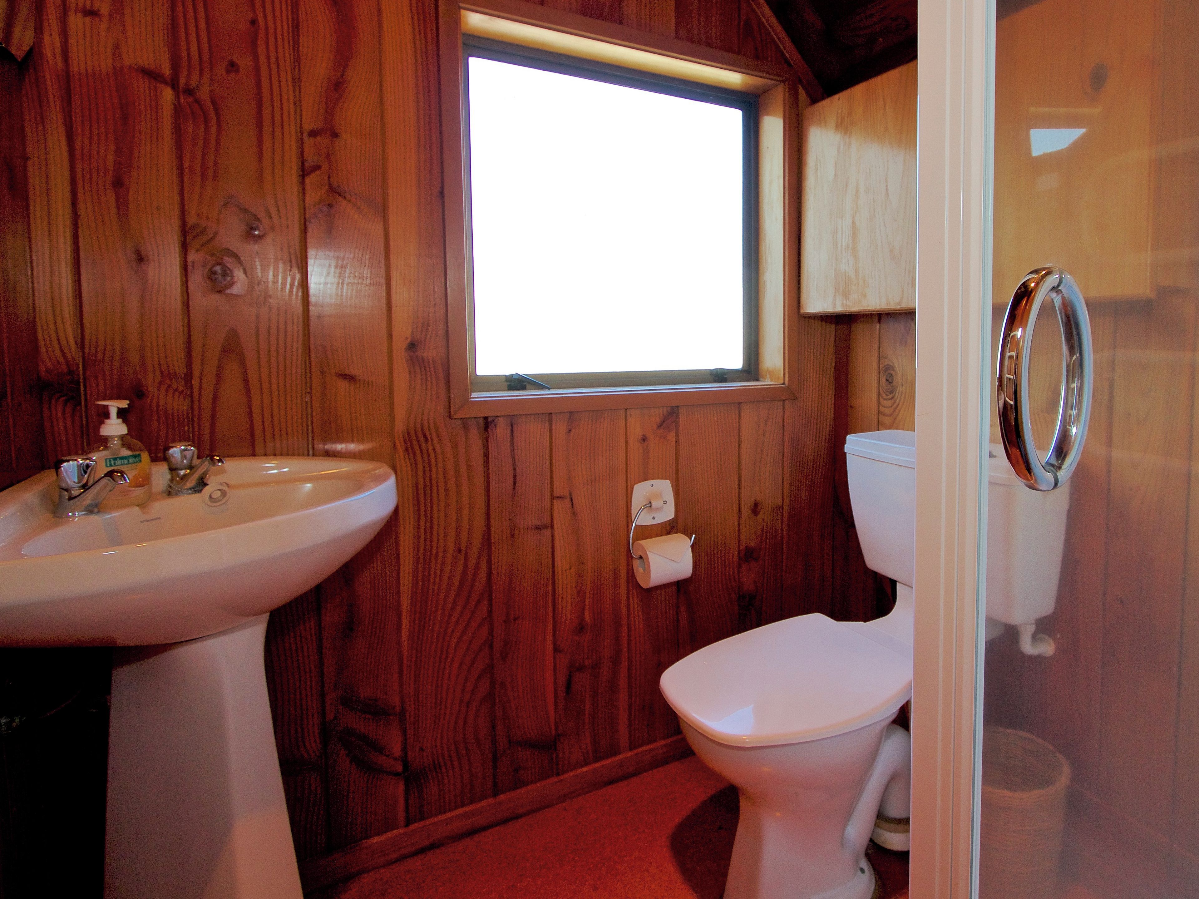 Een badkamer met houten wanden, een witte wastafel, een toilet en een raam.