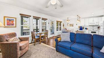 A living room with a blue sofa, a dining table with chairs, a ceiling fan, and a kitchen area with cabinets and appliances.