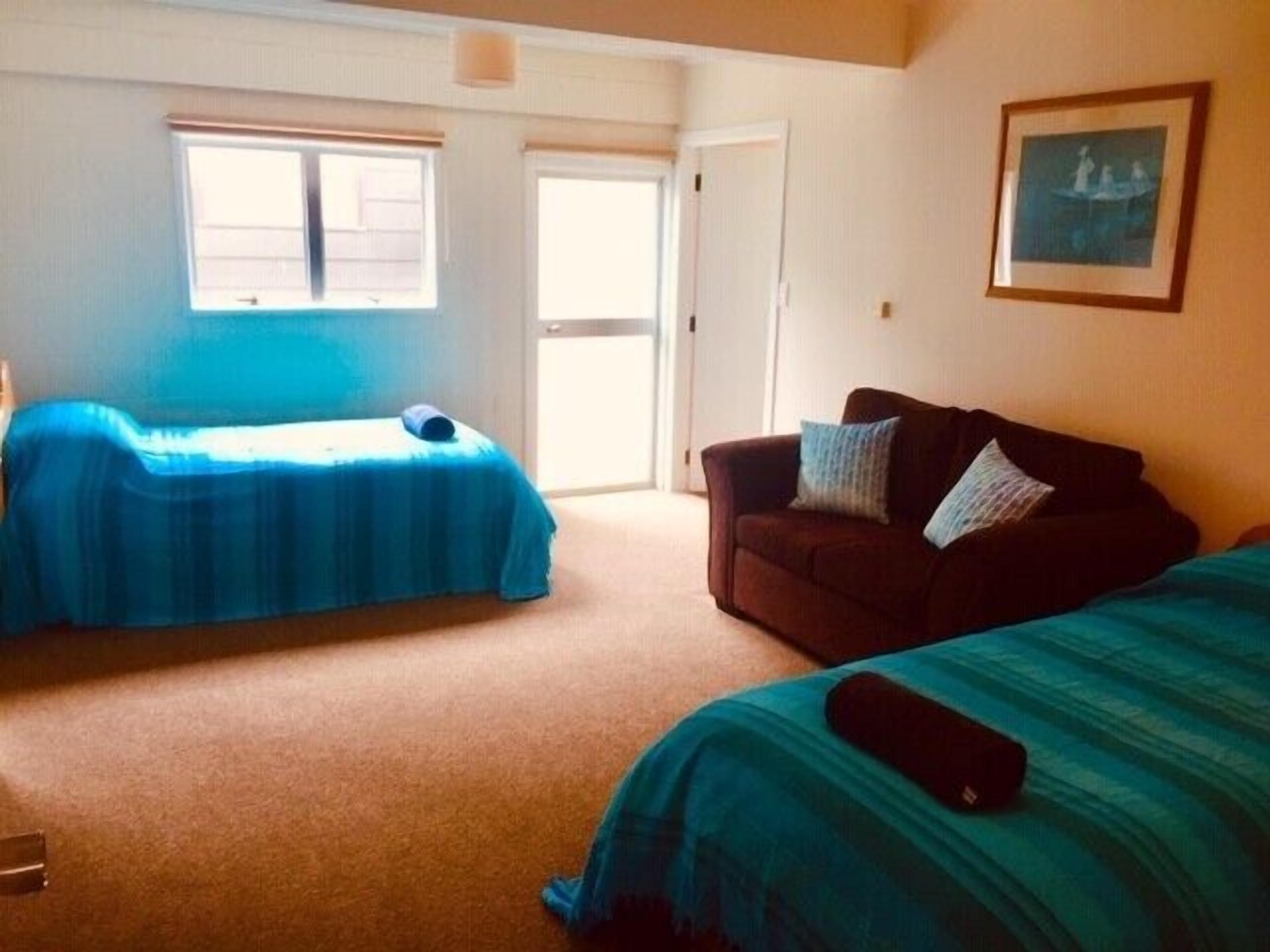 A room with two beds, a sofa, and a door leading to a balcony.