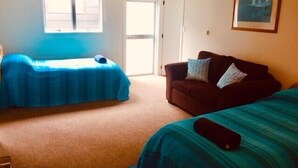 A room with two beds, a sofa, and a door leading to a balcony.
