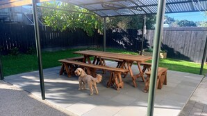 A covered patio area with wooden picnic tables and a small dog.