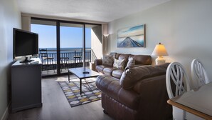 Una sala de estar con sofá, televisor y vista al mar a través de amplias ventanas.