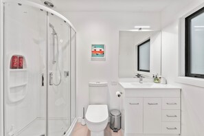 A modern bathroom with a glass-enclosed shower, a white toilet, a sink with a mirror, and a trash bin.