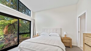 Een slaapkamer met een groot raam, een bed, twee nachtkastjes met lampen en een houten nachtkastje.