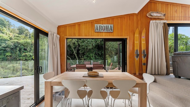 Een moderne eethoek met een houten tafel en witte stoelen, een houten plafond en uitzicht op het omliggende landschap.