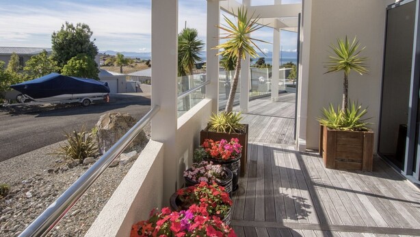 A balcony with potted plants and a view of the street. - Sun, Sea, Sensational - Kaiteriteri Holiday Home (Kaiteriteri)