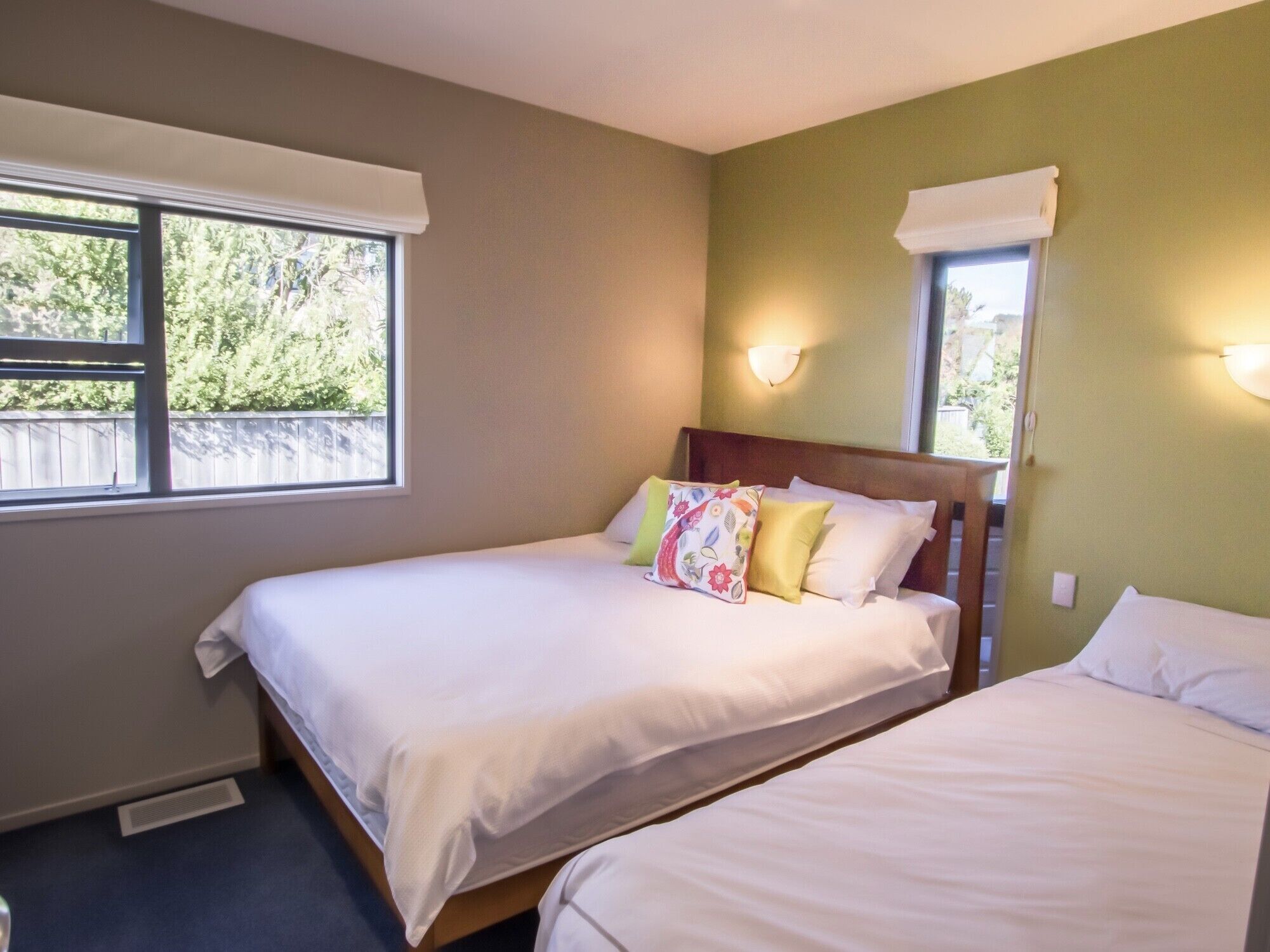 Habitación de hotel con dos camas individuales, una ventana con vistas a la vegetación y una lámpara fijada a la pared.