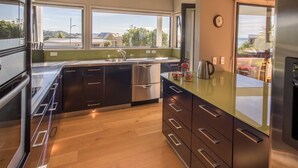 A modern kitchen with a large window, stainless steel appliances, and a view of the outdoors. - Sun, Sea, Sensational - Kaiteriteri Holiday Home (Kaiteriteri)