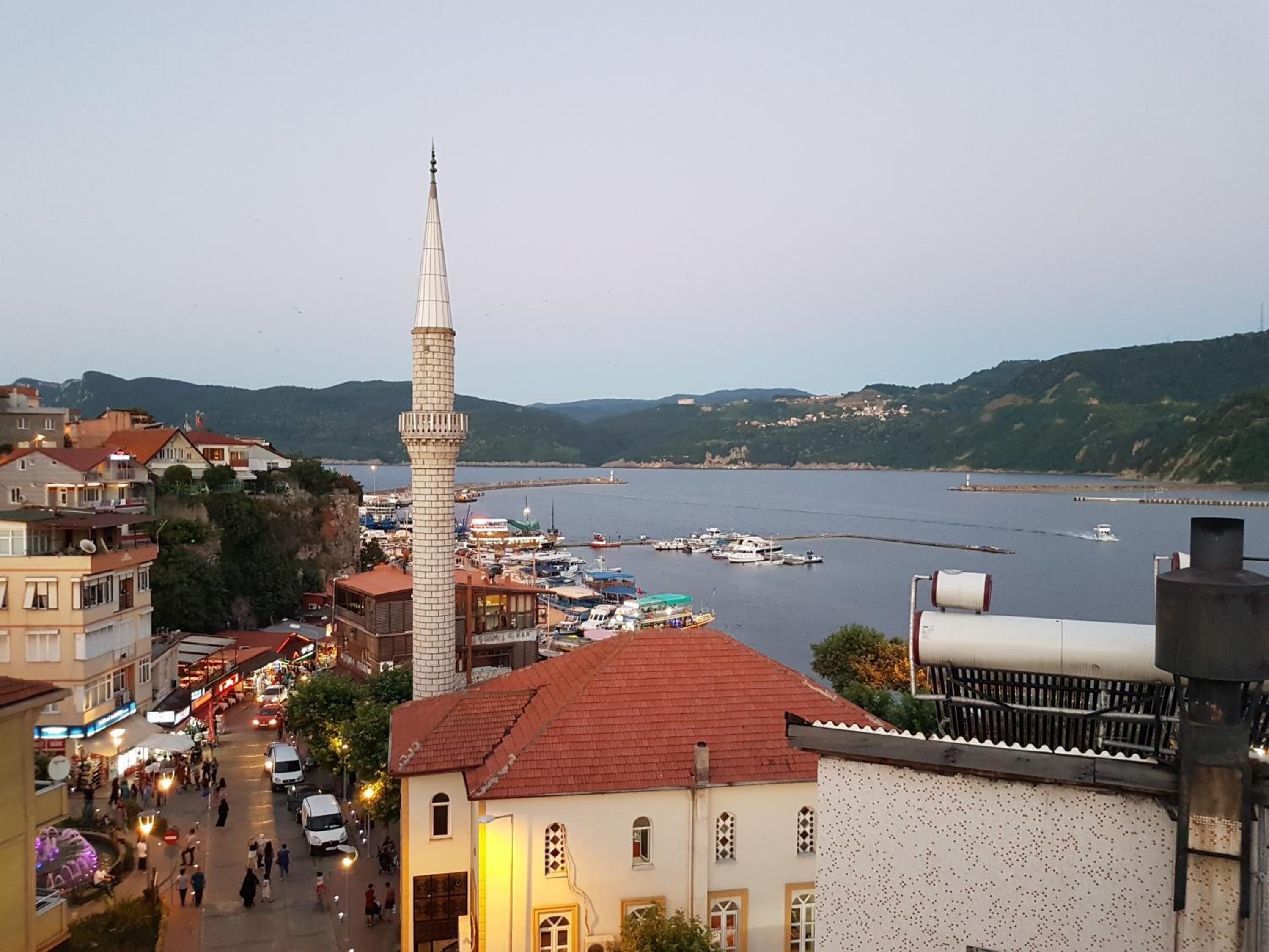 A coastal town with a prominent minaret, a marina with boats, and a bustling street with pedestrians and vehicles.