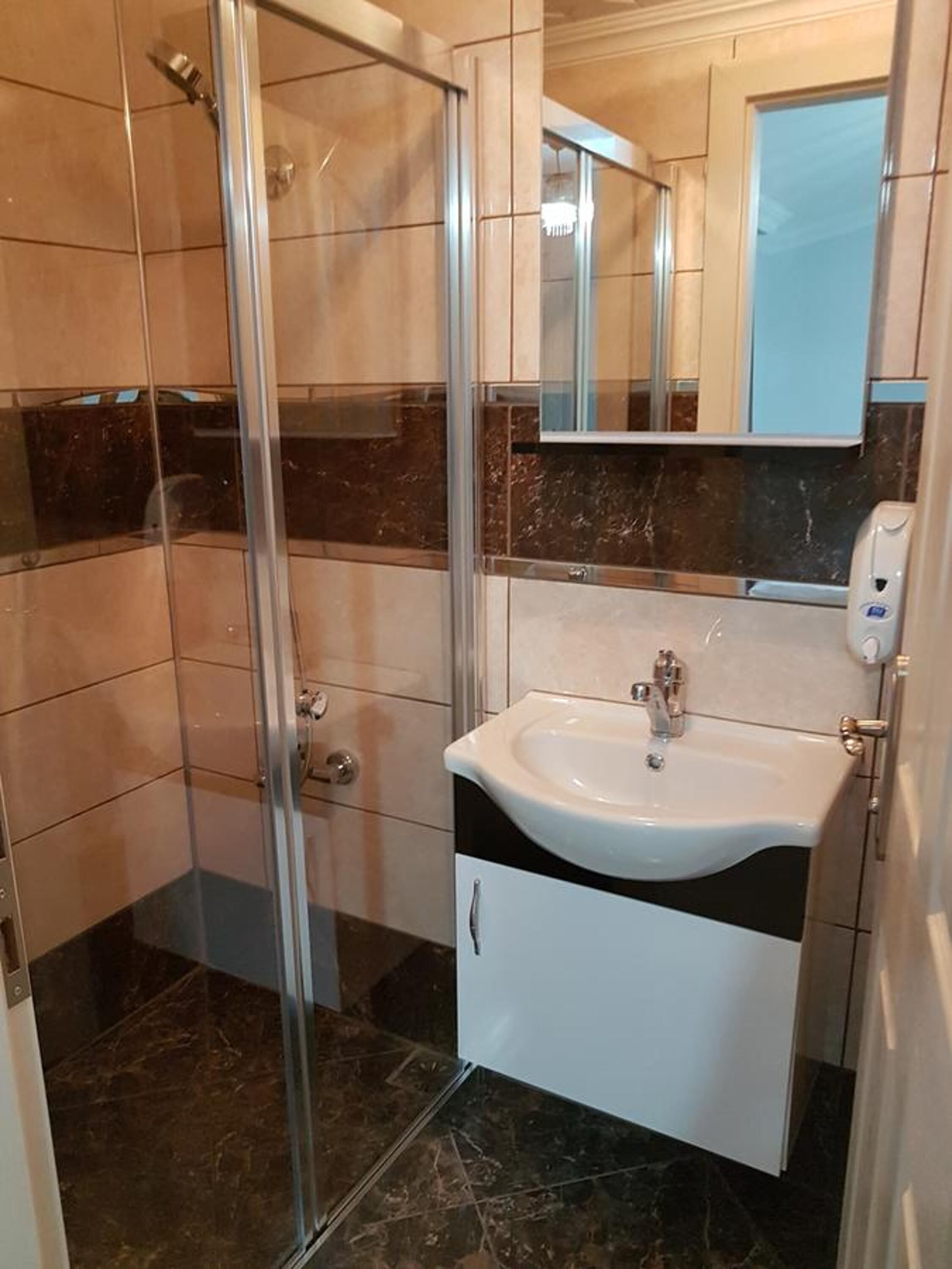 A bathroom with a glass shower enclosure, a white sink with a gold faucet, and a mirror above the sink.