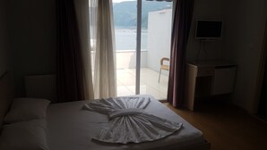 A hotel room with a bed, a desk, and a view of the sea. - Karadeniz Pansiyon (Amasra)