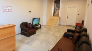 A living room with a sofa, a television, a wooden desk, and a staircase leading to another floor. - Karadeniz Pansiyon (Amasra)