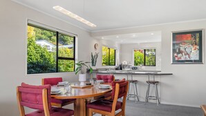 A modern kitchen with a dining area, large windows, and a view of greenery. - Acacia Views - Acacia Bay Holiday Home (Acacia Bay)