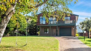 A two-story house with a front garage, a swing set, and a well-maintained lawn. - Acacia Views - Acacia Bay Holiday Home (Acacia Bay)
