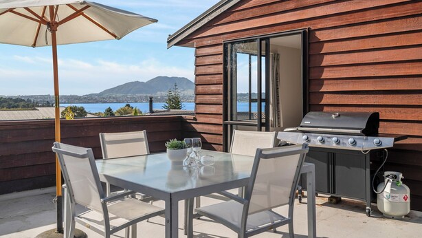 An outdoor patio with a table, chairs, a grill, and an umbrella. - Acacia Views - Acacia Bay Holiday Home (Acacia Bay)