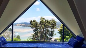Een kamer met een drielhoekig raam dat uitzicht biedt op een meer, bomen en verre bergen.