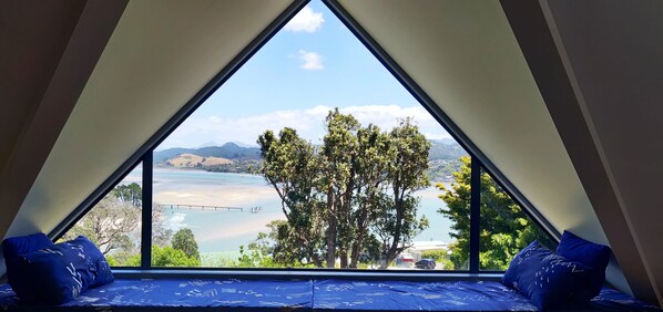 A room with a triangular window offering a view of a lake, trees, and distant mountains.