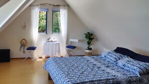 Een gezellig slaapkamer op zolder met een schuine plafond, een groot bed met beddengoed met dessin, een tafeltje met decoratieve objecten, een stoel en een potplant.