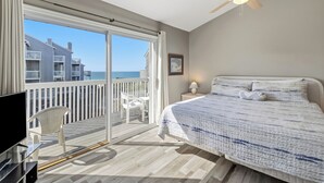 A bedroom with a bed, a TV, a ceiling fan, a balcony with a chair, and a view of buildings and the sea. - SEACLUSION OFFERS GULF VIEWS & STEPS TO BEACH! 2 COMMUNITY POOLS! (Port Saint Joe)