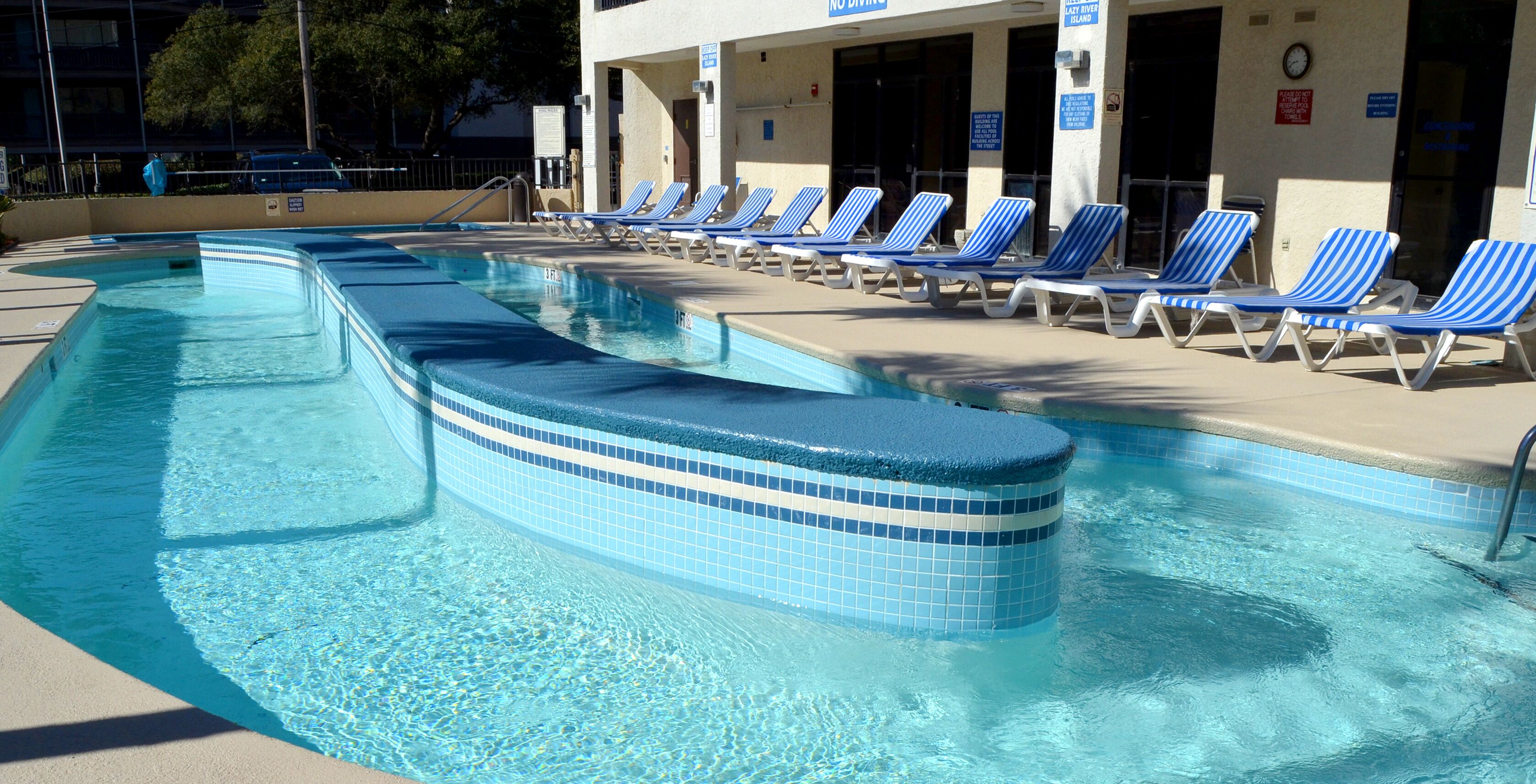 A swimming pool with blue and white tiled edges, surrounded by lounge chairs and a building with a sign that reads "No Diving".