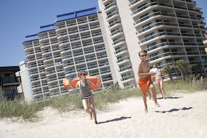 Un hotel frente a la playa con varios balcones y una playa arenosa en primer plano.