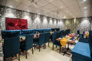 Een restaurant met blauwe bekleden zitbanken en tafels, een rood gordijn en een bloemenpatroon op de muur.