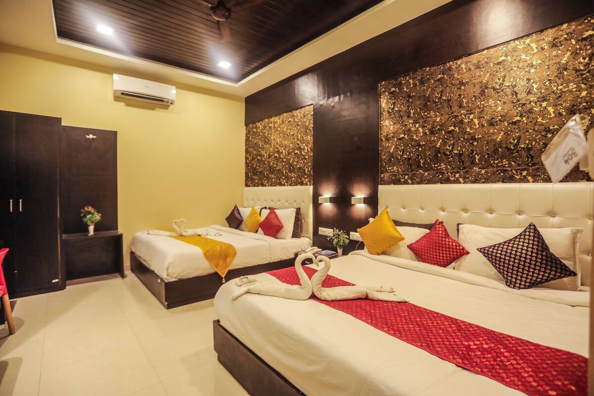Habitación de hotel con dos camas, cada una con ropa blanca y almohadas decorativas. Una cama tiene una manta roja y el mesita de noche sostiene una pequeña planta en maceta.
