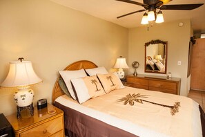Quarto com cama, duas mesas de cabeceira, criadeira, ventoinha no teto, espelho e cômoda.