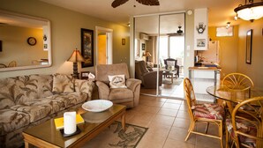 A living room with a sofa, armchair, coffee table, and dining area with chairs and a table. - Nani Kai Hale #304 on Sugar Beach (Kihei)