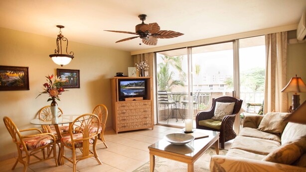A living room with a ceiling fan, a television, a dining area with chairs, a sofa, and a view through large sliding glass doors. - Nani Kai Hale #304 on Sugar Beach (Kihei)
