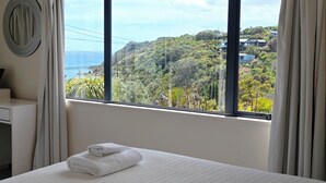 A hotel room with a large window offering a view of a hillside and ocean.