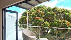 A balcony with wicker furniture and a glass railing overlooking a garden with red flowers.